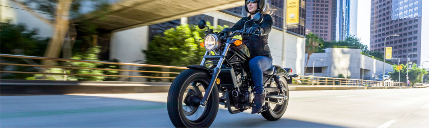 A person driving a Honda® motorcycle in the city while going underneath a bridge